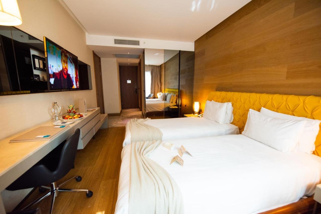 Dosso Dossi Hotels & Spa Downtown Istanbul Luaran gambar The photo shows a modern hotel room featuring two single beds with white linens. There is a stylish yellow accent wall behind the beds. A flat-screen television is mounted on the wall opposite the beds, and a sleek desk and chair are positioned next 