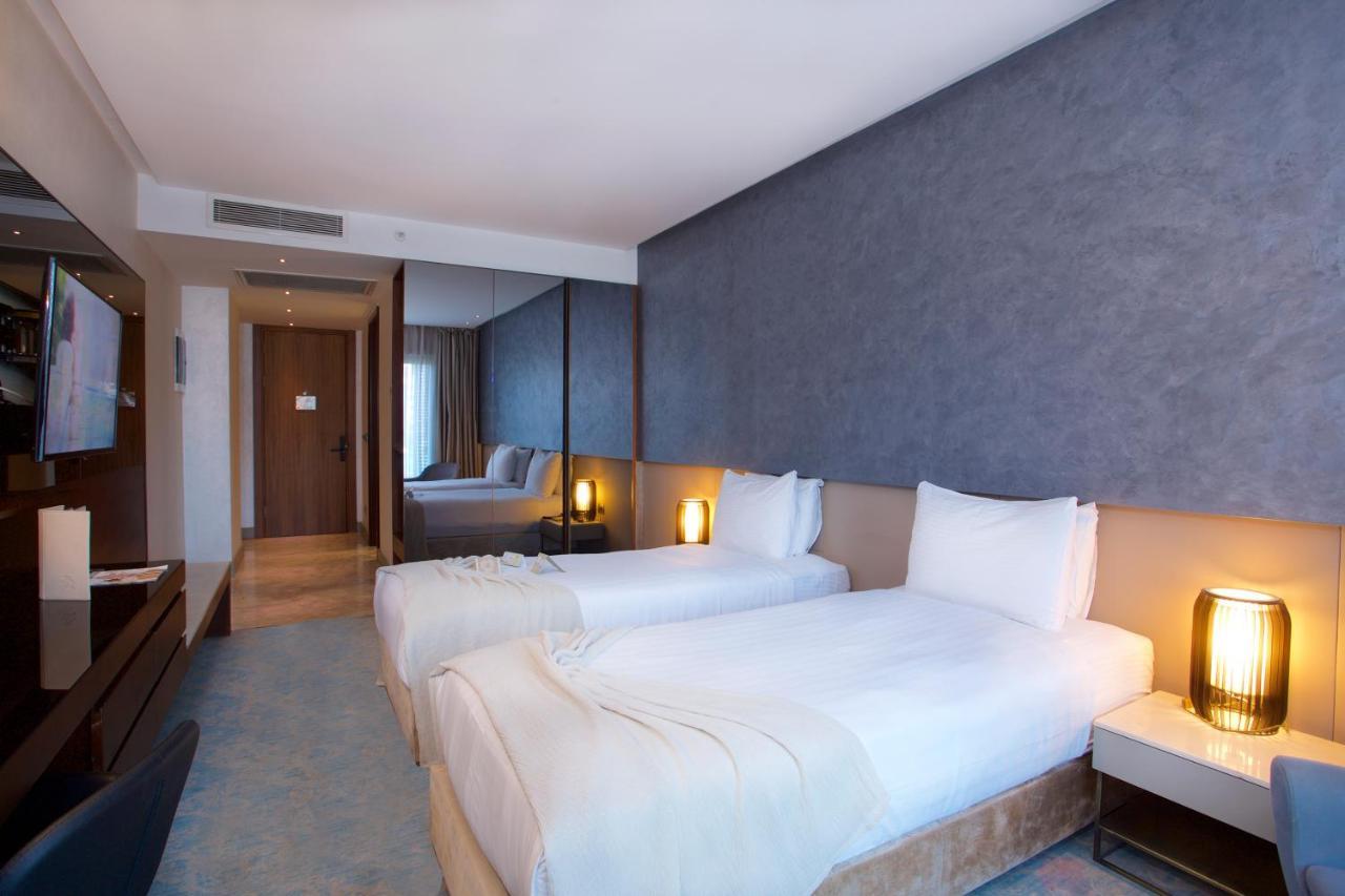 Dosso Dossi Hotels & Spa Downtown Istanbul Luaran gambar The photo shows a modern hotel room featuring two single beds with white bedding. The walls have a stylish gray finish, and there is a decorative element behind the beds. On either side of the beds, there are bedside tables with lamps. A flat-screen 